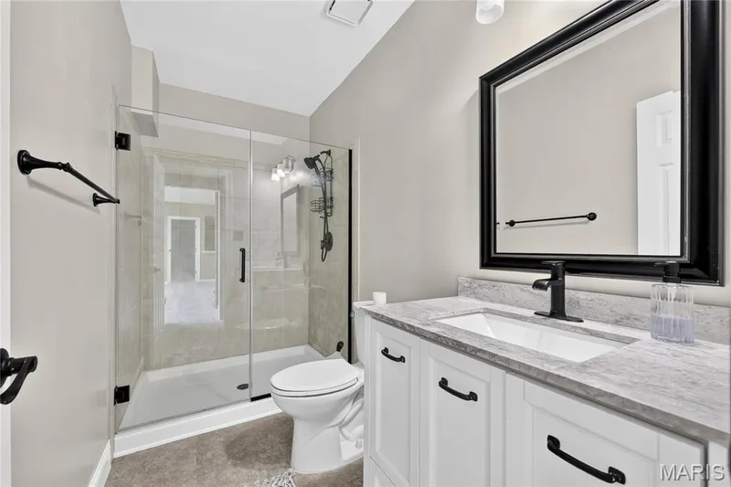 Glass-enclosed shower with tile surround, single vanity with integrated sink, stone countertop, and large framed mirror — 17711 Birch Leaf Court, Chesterfield, MO 63005