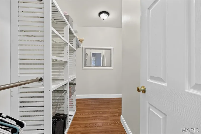 Built-in closet shelving system with a hanging rod, wood-finish flooring, and white paneled door with brass hardware — 17711 Birch Leaf Court, Chesterfield, MO 63005