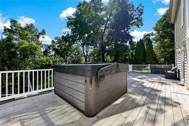 Spacious outdoor deck featuring a hot tub, white railing, exterior wall lighting, and natural surroundings — 17711 Birch Leaf Court, Chesterfield, MO 63005