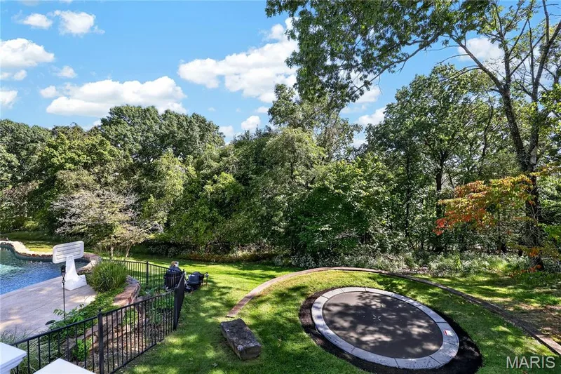 Expansive landscaped yard with a built-in trampoline, manicured lawn, and a fenced swimming pool area — 17711 Birch Leaf Court, Chesterfield, MO 63005