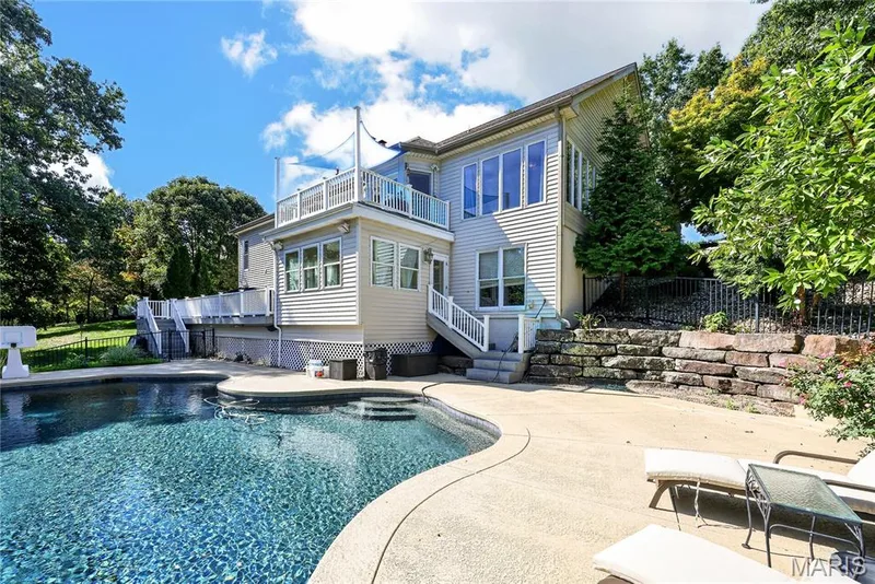 In-ground swimming pool with integrated steps, concrete patio, multi-level deck with white railings, and stacked stone retaining walls — 17711 Birch Leaf Court, Chesterfield, MO 63005