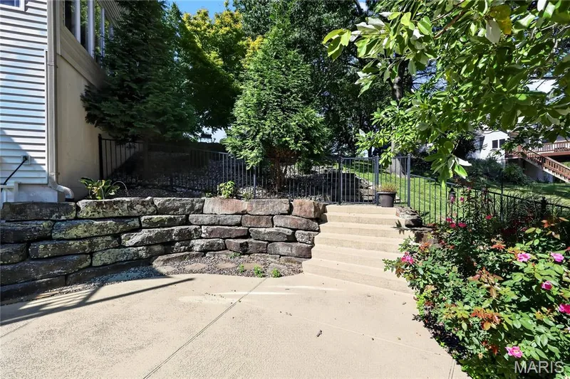 Concrete patio area with a stone retaining wall, concrete steps, and black metal fencing — 17711 Birch Leaf Court, Chesterfield, MO 63005