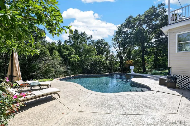 Freeform swimming pool with integrated steps, surrounded by a stamped concrete patio, and mature trees providing a natural backdrop — 17711 Birch Leaf Court, Chesterfield, MO 63005