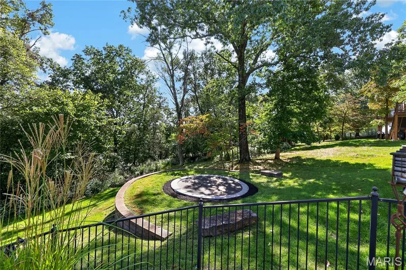 Spacious grassy yard featuring mature trees, a circular paved patio, and a curved retaining wall — 17711 Birch Leaf Court, Chesterfield, MO 63005