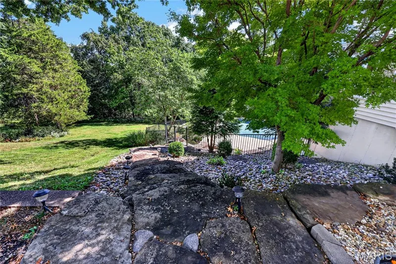 Expansive outdoor area featuring a stone pathway, mature trees, manicured lawn, and a fenced pool area — 17711 Birch Leaf Court, Chesterfield, MO 63005