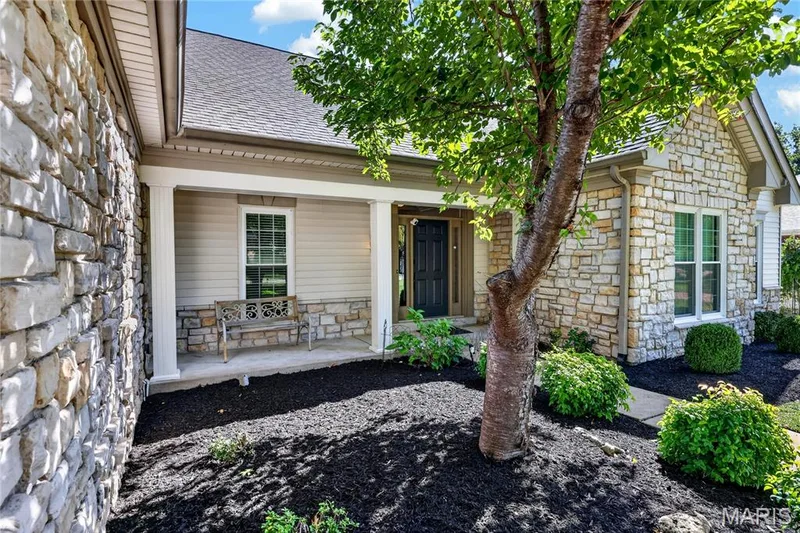 Stone veneer exterior with siding accents, covered front porch, dark-paneled entry door, and manicured landscaping — 17711 Birch Leaf Court, Chesterfield, MO 63005