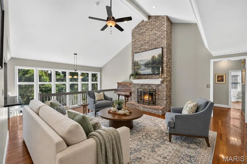 Vaulted ceilings with crown molding, full-height brick fireplace with a decorative mantel, wood-finish flooring, and expansive multi-pane windows — 17711 Birch Leaf Court, Chesterfield, MO 63005