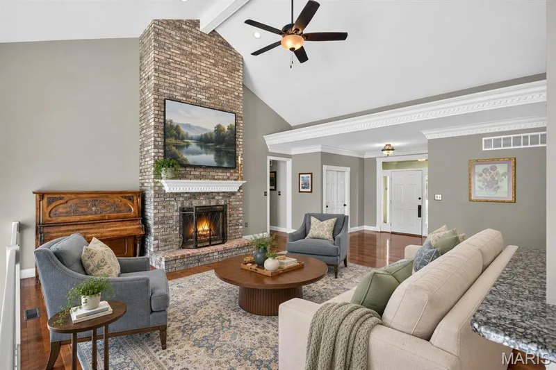 Vaulted ceilings featuring decorative crown molding, full-height masonry fireplace with a white mantel, and wood-finish flooring — 17711 Birch Leaf Court, Chesterfield, MO 63005