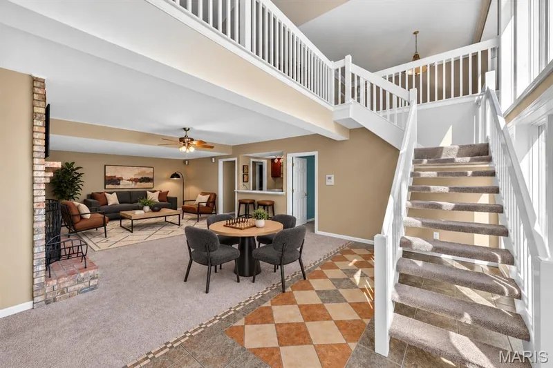 Open-concept interior featuring vaulted ceilings, a brick-surround fireplace, a white wooden staircase railing, and tile flooring with a geometric inlay pattern — 17711 Birch Leaf Court, Chesterfield, MO 63005