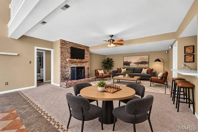 Floor-to-ceiling brick fireplace with a custom mantel, neutral wall-to-wall carpeting, tiered ceiling detail, and a breakfast bar — 17711 Birch Leaf Court, Chesterfield, MO 63005