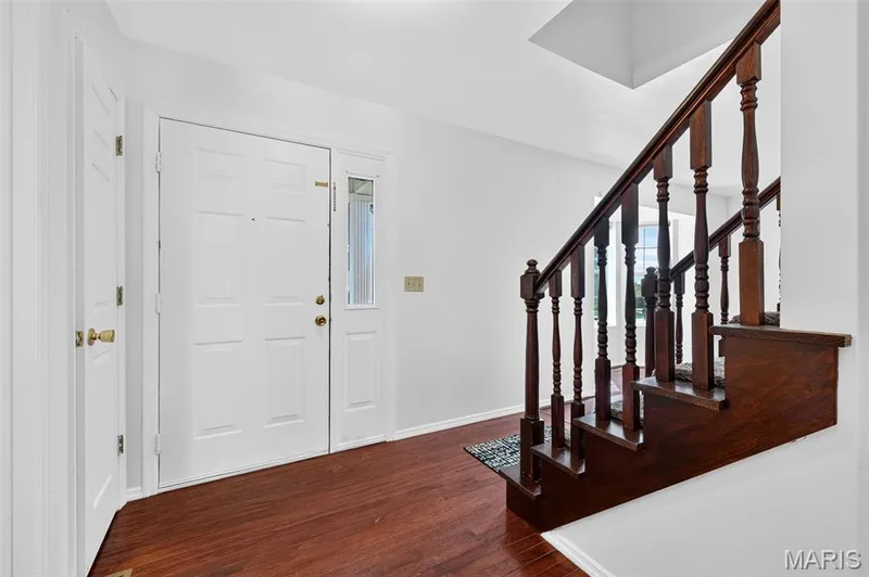 Entryway featuring wood-finish flooring, a paneled front door with sidelight, and a wooden staircase with turned balusters — 39 Green Pines Circle, St Peters, MO 63376