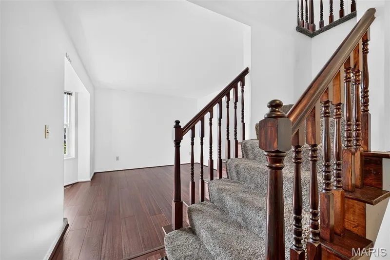 Wood-finish flooring, carpeted staircase, wood banister with ornate spindles, and white wall finishes — 39 Green Pines Circle, St Peters, MO 63376