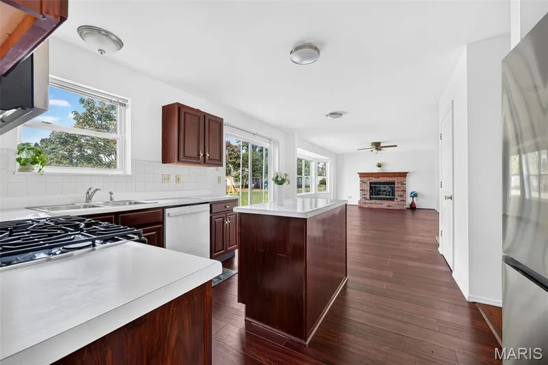 Kitchen featuring a gas range, white countertops, dark wood cabinetry, a center island, and a tile backsplash — 39 Green Pines Circle, St Peters, MO 63376
