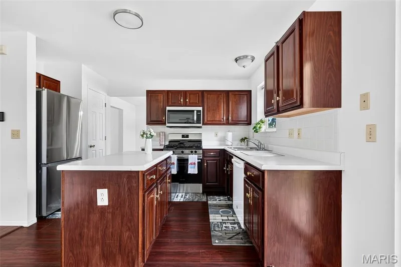 Kitchen featuring wood-finish flooring, dark wood cabinetry, white countertops, and a white subway tile backsplash — 39 Green Pines Circle, St Peters, MO 63376