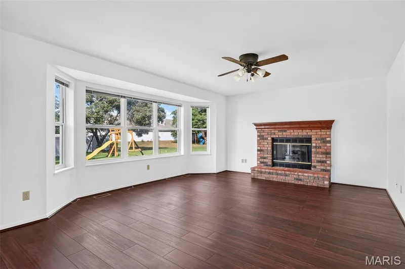 Wood-finish flooring throughout, brick fireplace with wood mantel, ceiling fan with integrated lighting, and a bay window with multiple panes — 39 Green Pines Circle, St Peters, MO 63376