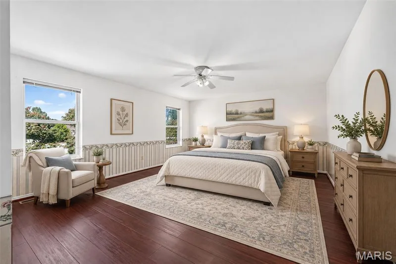 Deep-toned wood-finish flooring, two large windows, ceiling fan, and white walls — 39 Green Pines Circle, St Peters, MO 63376