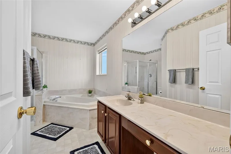 Spacious bathroom featuring a built-in corner soaking tub, a separate shower enclosure, a long vanity with dual sinks, and an expansive wall-mounted mirror — 39 Green Pines Circle, St Peters, MO 63376