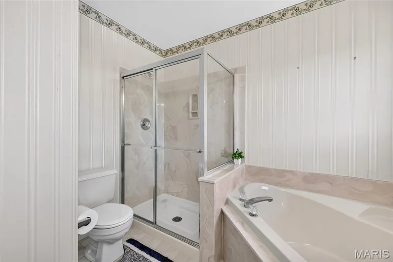 White paneled walls with decorative border, glass-enclosed shower, soaking tub, and tile flooring — 39 Green Pines Circle, St Peters, MO 63376