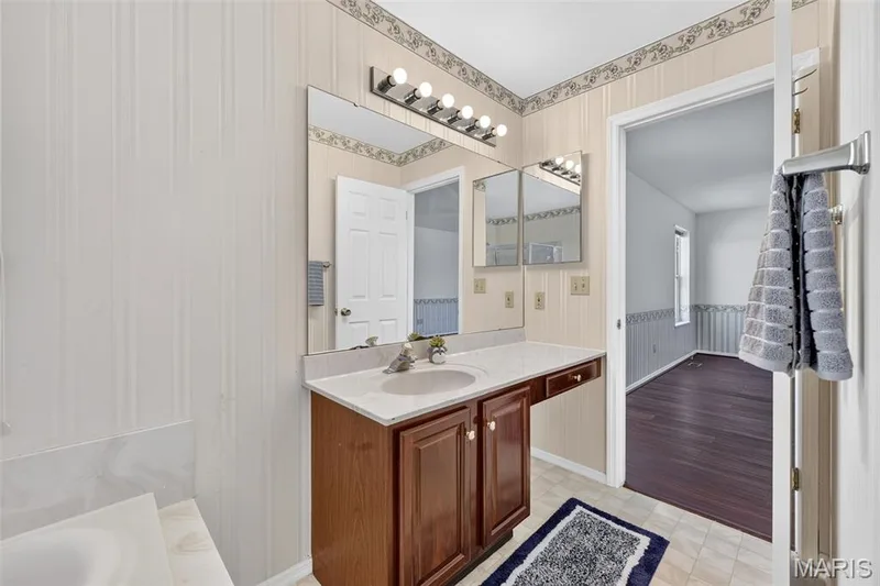 Vanity with a single basin sink, light-colored countertop, wood-finish cabinetry, and wall-mounted lighting fixture — 39 Green Pines Circle, St Peters, MO 63376