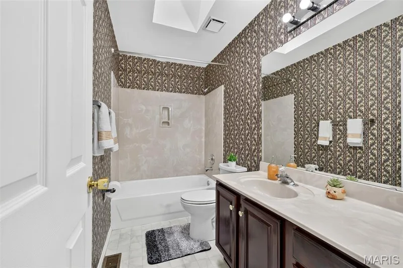Bathroom featuring a built-in tub with a shower, a vanity with an integrated sink, a large wall-mounted mirror, and overhead lighting — 39 Green Pines Circle, St Peters, MO 63376