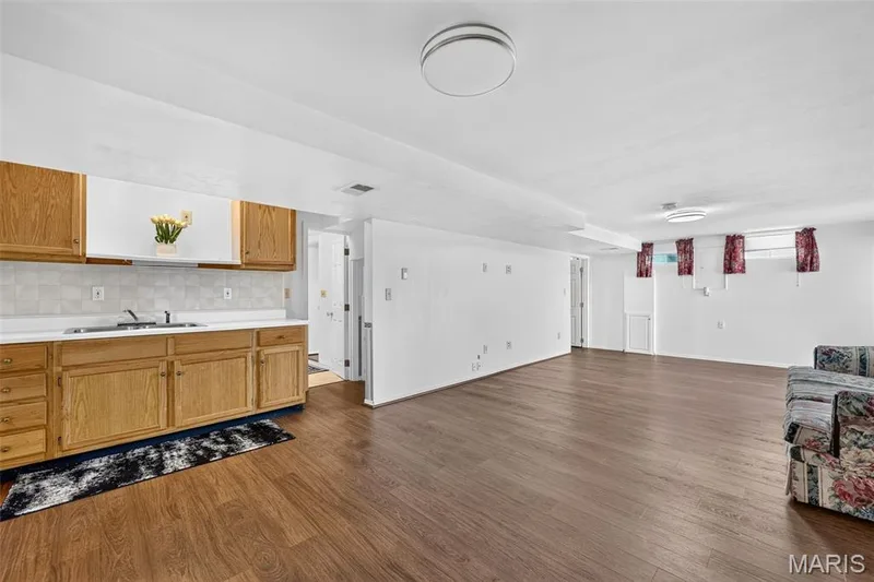 Wood-finish flooring throughout, kitchenette with wood cabinetry, tile backsplash, and stainless steel sink — 39 Green Pines Circle, St Peters, MO 63376