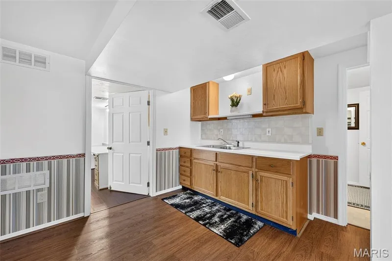 Kitchenette featuring wood-finish flooring, wood cabinetry, a stainless steel sink, and a white countertop with a tiled backsplash — 39 Green Pines Circle, St Peters, MO 63376