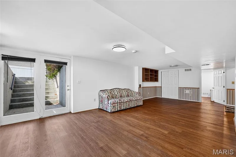Spacious room featuring wood-finish flooring, white walls, built-in shelving, and a glass-paneled exterior door with an exterior staircase — 39 Green Pines Circle, St Peters, MO 63376