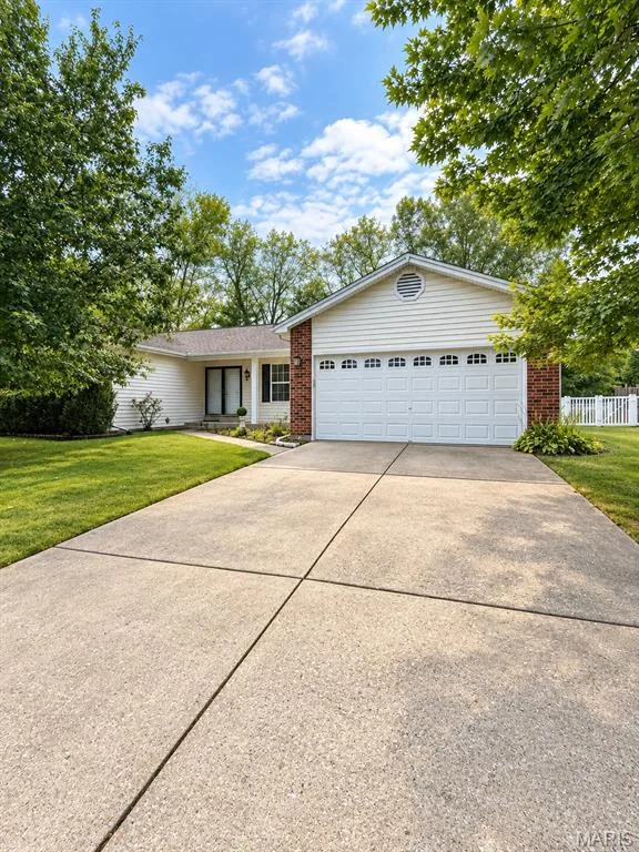Exterior featuring white siding, brick accents, a two-car garage, mature trees, and a concrete driveway — 3 Fairfax Drive, St Peters, MO 63376