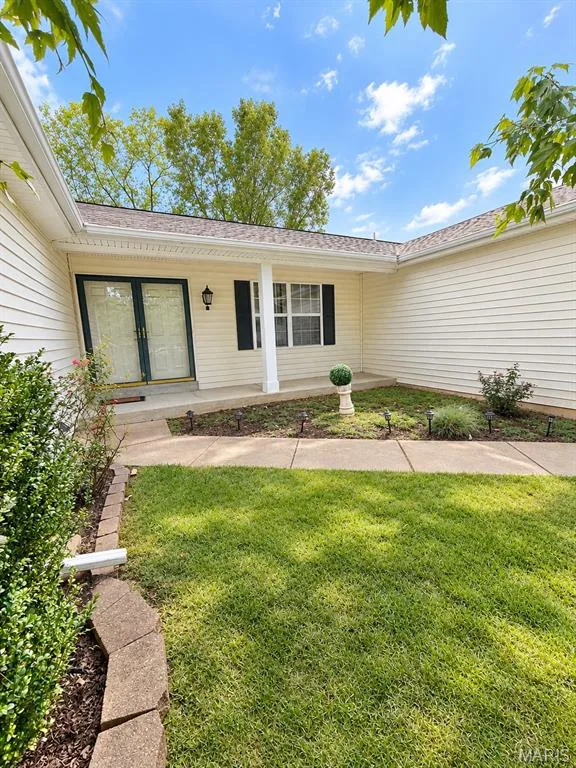 Exterior featuring light-colored siding, a covered entry with a white column, dark shutters, and a well-maintained lawn with a concrete pathway — 3 Fairfax Drive, St Peters, MO 63376