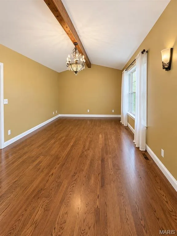 Vaulted ceiling with exposed wood beam, hardwood flooring, and decorative chandelier — 3 Fairfax Drive, St Peters, MO 63376