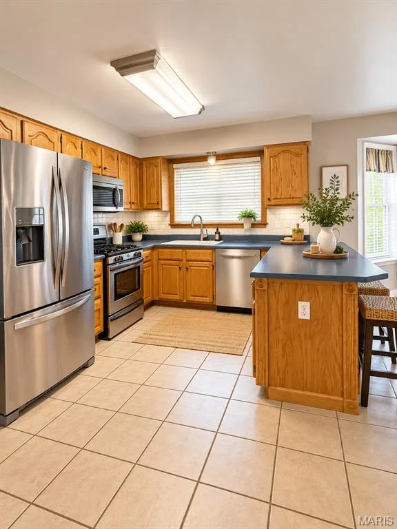 Kitchen featuring wood cabinetry, stainless steel appliances, a tile backsplash, durable countertops, and tile flooring — 3 Fairfax Drive, St Peters, MO 63376