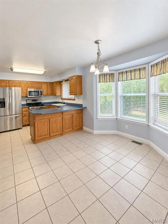 Kitchen area featuring wood cabinetry, stainless steel appliances, ceramic tile flooring, and a bay window — 3 Fairfax Drive, St Peters, MO 63376