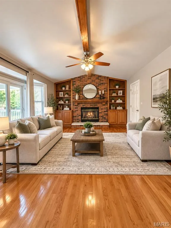 Hardwood flooring, brick fireplace with mantel, built-in shelving, ceiling fan, and large windows, virtually staged — 3 Fairfax Drive, St Peters, MO 63376