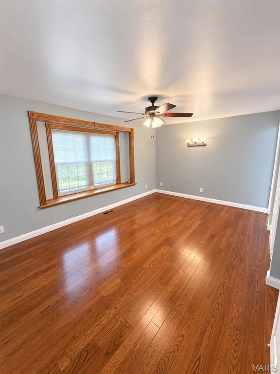 Wood-finish flooring throughout, ceiling-mounted fan with integrated lighting, wall-mounted light fixture, and window with wood trim — 3 Fairfax Drive, St Peters, MO 63376