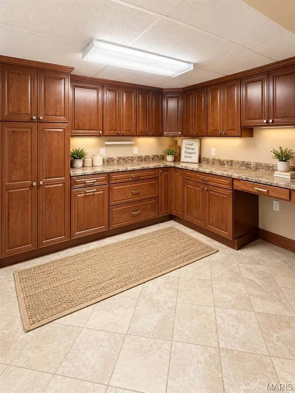 Downstairs partial kitchen with wood-finish cabinetry with polished hardware, stone-look countertops, tiled flooring, and under-cabinet lighting — 3 Fairfax Drive, St Peters, MO 63376