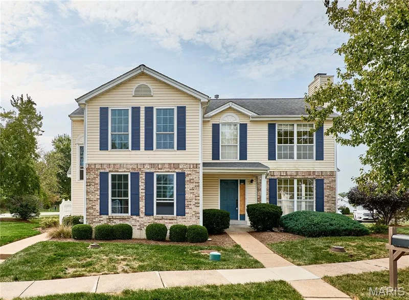 Two-story exterior with light-colored siding and brick accents, featuring multiple windows with dark shutters, a front entry door, and a gabled roof — 16500 Victoria Crossing Drive, Wildwood, MO 63040
