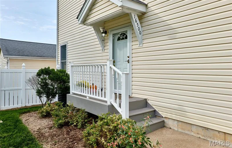 Welcoming front entry featuring a covered stoop with white railings, concrete steps, and a paneled entry door with transom window — 16500 Victoria Crossing Drive, Wildwood, MO 63040