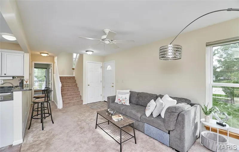 Open-concept living area with carpet flooring, a ceiling fan, and a kitchen pass-through with bar seating — 16500 Victoria Crossing Drive, Wildwood, MO 63040