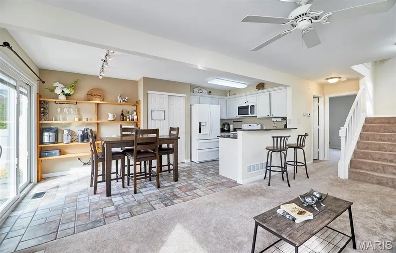Open-concept living space featuring a ceiling fan, white kitchen cabinetry, a kitchen peninsula with bar seating, and a sliding glass door — 16500 Victoria Crossing Drive, Wildwood, MO 63040