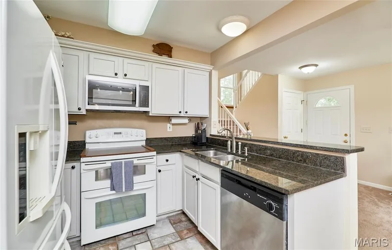White cabinetry, dark stone countertops, stainless steel dishwasher, and built-in microwave — 16500 Victoria Crossing Drive, Wildwood, MO 63040