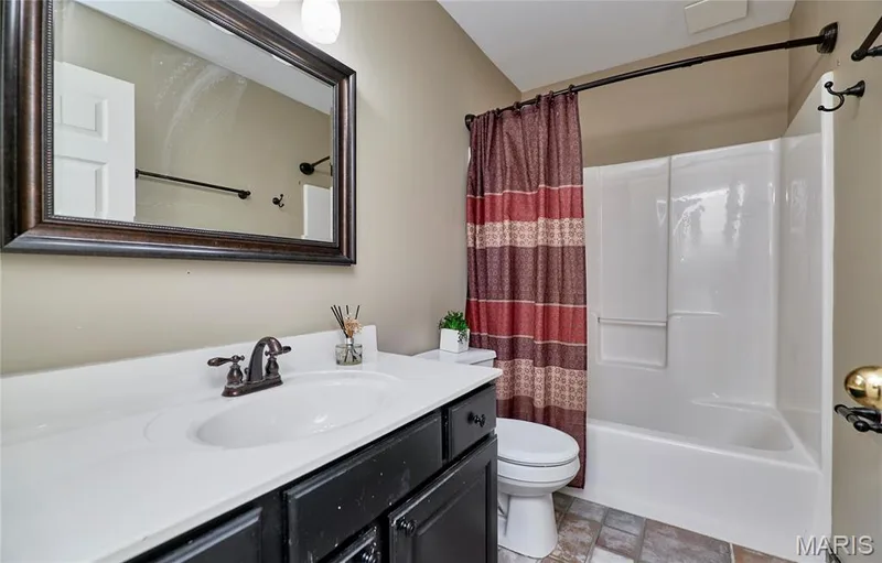 Vanity with a white countertop and bronze-finish faucet, framed mirror, toilet, and a shower-tub combination unit — 16500 Victoria Crossing Drive, Wildwood, MO 63040