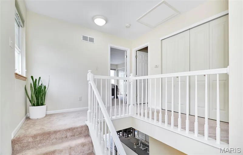 Carpeted landing featuring a window, built-in closet with bi-fold doors, and a white wood railing — 16500 Victoria Crossing Drive, Wildwood, MO 63040