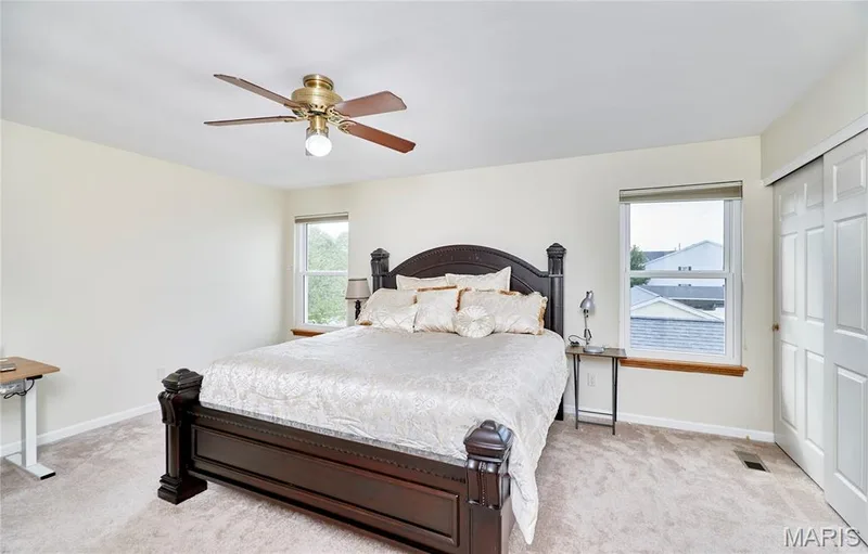 Carpeted bedroom featuring two windows with wood sills, a ceiling fan with light fixture, and a white bi-fold closet door — 16500 Victoria Crossing Drive, Wildwood, MO 63040
