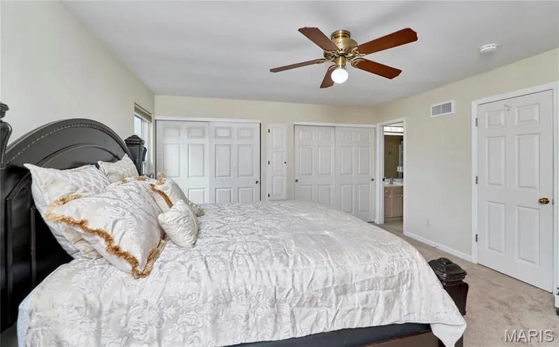 Bedroom featuring carpet flooring, a ceiling fan with integrated lighting, and two sets of sliding panel closet doors — 16500 Victoria Crossing Drive, Wildwood, MO 63040