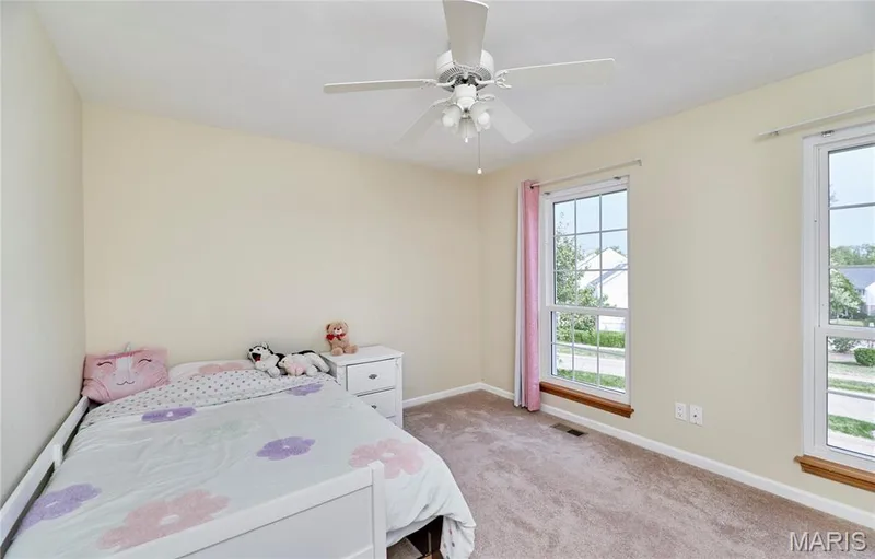 Carpeted room featuring a ceiling fan with integrated lighting, two double-hung windows, and light-toned wall finishes — 16500 Victoria Crossing Drive, Wildwood, MO 63040