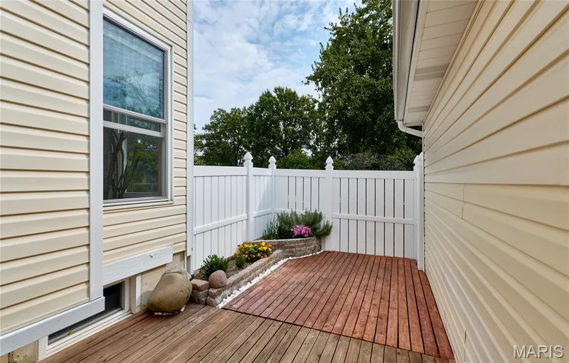Exterior deck featuring wood-finish boards, white privacy fencing, and stone-edged planter beds — 16500 Victoria Crossing Drive, Wildwood, MO 63040