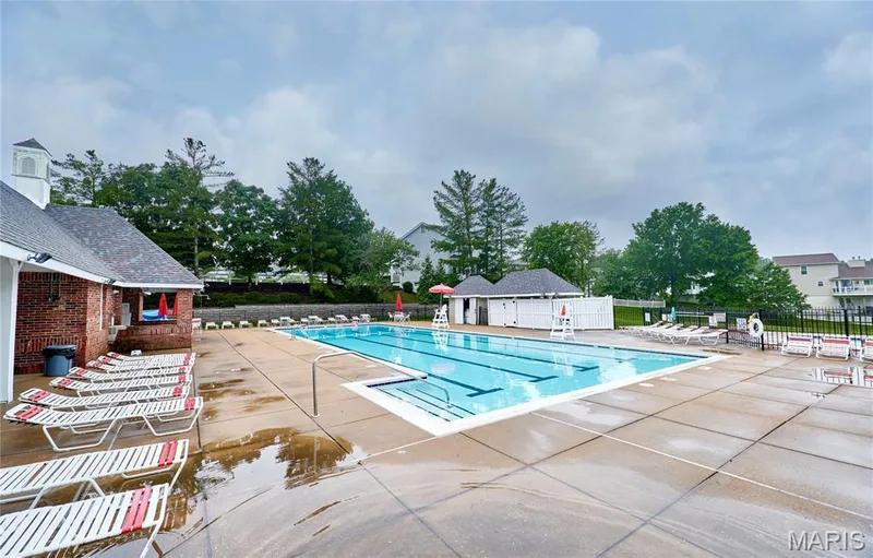 Community swimming pool with lap lanes, expansive concrete decking, and an adjacent brick clubhouse featuring a white cupola — 16500 Victoria Crossing Drive, Wildwood, MO 63040