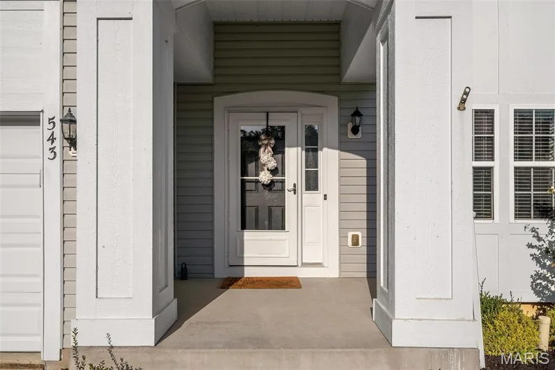 Entryway with a storm door, two exterior sconce lights, concrete porch, and horizontal siding — 543 Country Chase Drive, Lake St. Louis, MO 63367