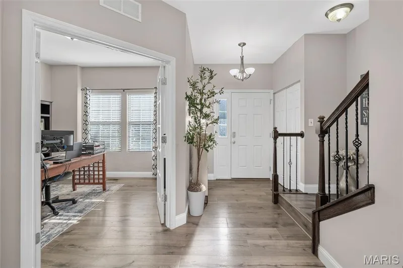 Wood-finish flooring throughout, entry door with decorative glass, and a staircase featuring dark wood newel posts and wrought iron balusters — 543 Country Chase Drive, Lake St. Louis, MO 63367