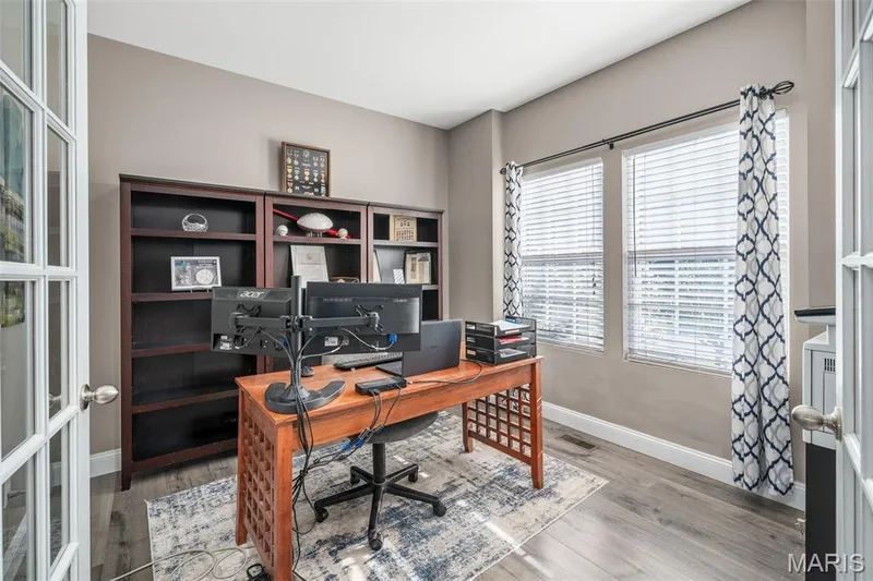 French doors with grid-patterned glass panels, built-in shelving, two large windows, wood-finish flooring, and neutral wall paint — 543 Country Chase Drive, Lake St. Louis, MO 63367
